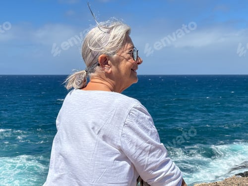 Preview: Senior white haired woman sitting face the sea relaxing and admiring the horizon