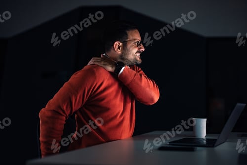 Preview: A man having a back pain while working at the office, late at night.