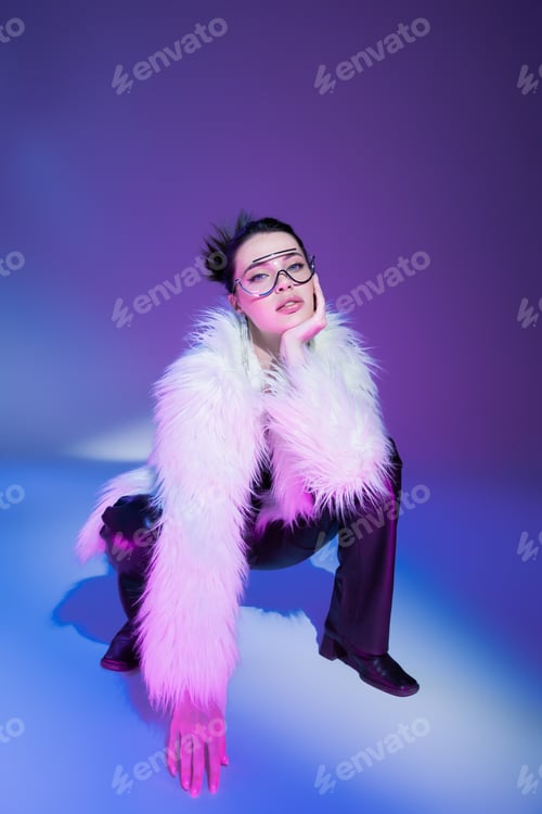 Preview: trendy woman in transparent eyeglasses and white fluffy jacket looking at camera on purple