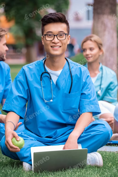 Preview: handsome asian medical student holding apple with laptop and looking at camera