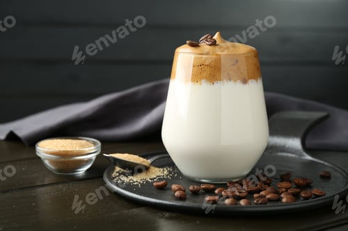 Preview: Delicious dalgona coffee in glass, beans and brown sugar on wooden table, closeup