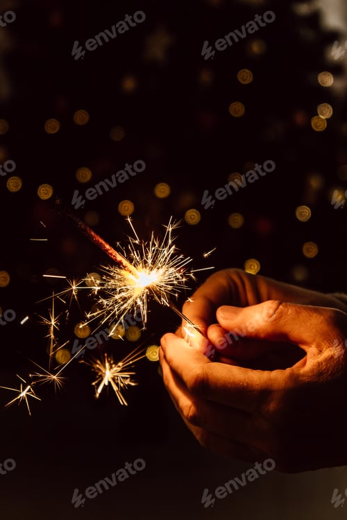 Preview: Bright festive Christmas sparkler in men's hands on the background of the Christmas tree. Close-up.