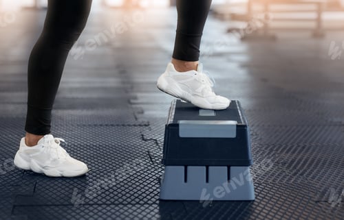 Preview: Cropped view of young woman in sports shoes doing exercises with step platform at gym, closeup