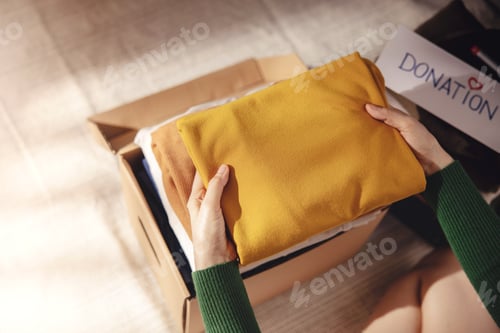 Preview: Clothes Donation Concept. Box of Cloth with Donate label. Woman Preparing Used Old Garment