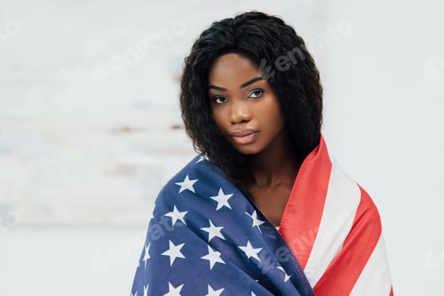 Preview: african american woman covered with flag of american looking at camera