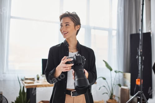 Preview: merry female photographer in casual clothes with camera in her hands smiling and looking away