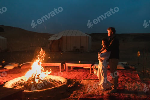 Preview: Couple hug in love near big campfire. Romantic night in glamping desert camp in Sahara, Morocco