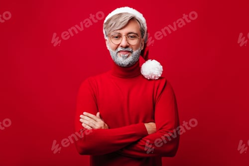 Preview: Handsome old man in glasses and santa claus hat posing in studio. Indoor portrait of male model iso