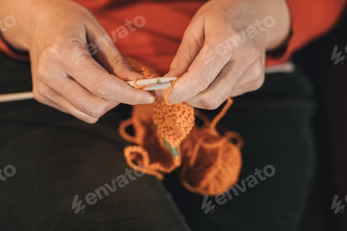 Preview: High angle view of a woman's hands knitting with two needles sitting on the couch