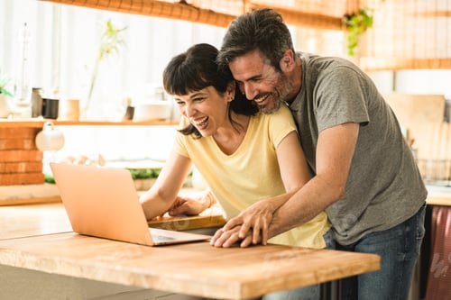 Preview: Smiling mature couple in the kitchen at home and having fun shopping online on the computer together