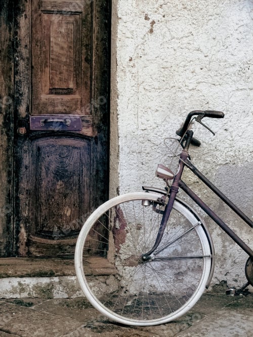 Preview: Vintage bicycle leaning against a weathered wall next to an old wooden door