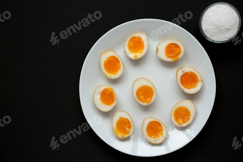 Preview: Homemade Unami Soy Sauce Eggs on a white plate on a black surface, top view.