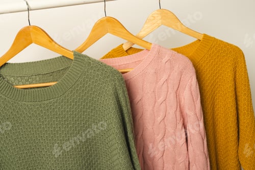 Preview: Three sweaters hanging from clothes rail with copy space on white background