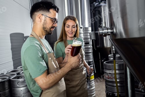 Preview: Man and woman working in craft brewery examining quality of the beer.