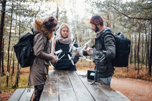 Preview: Group of three students tuning quadcopter at table in forest
