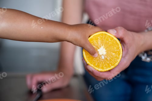Preview: Close-up view of a child's finger pressing into a juicy half of an orange held by an adult.