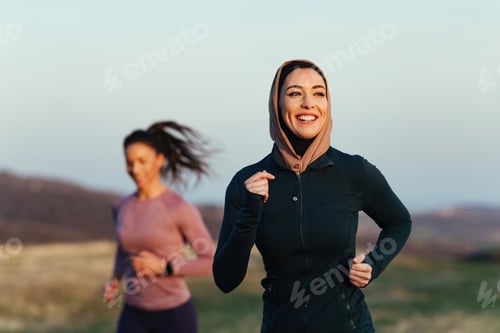 Preview: Happy female athlete jogging in the morning with personal trainer in nature.