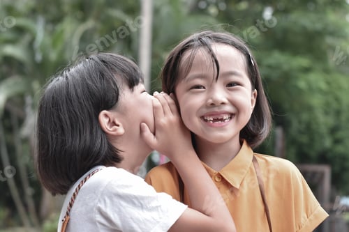 Preview: Two little sister girls whisper in ear at park outdoor.