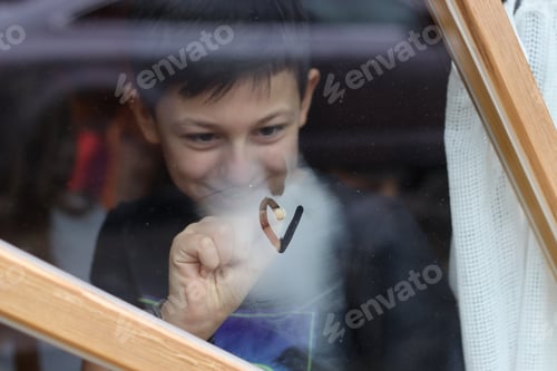 Preview: The boy is painting on the window with his finger.