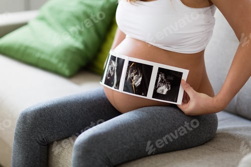 Preview: Pregnant woman holding ultrasound photo on belly