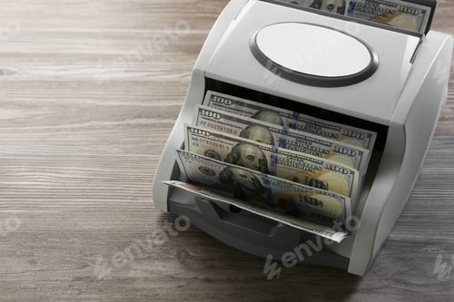 Preview: Money counter machine with dollar banknotes on wooden table, closeup. Space for text