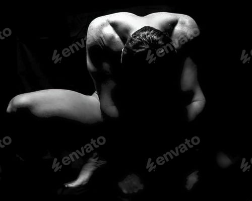 Preview: Naked male fitness model in yoga pose looking down on a black background