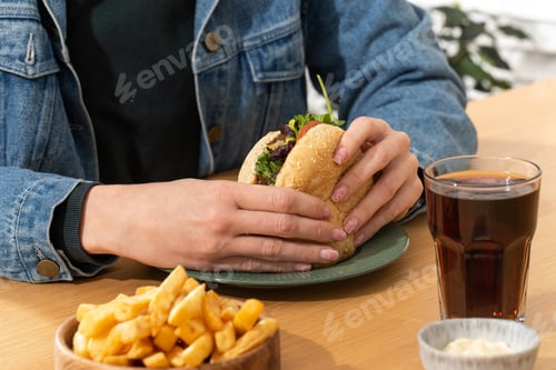 Preview: Woman eats delicious hamburger with french fries at table