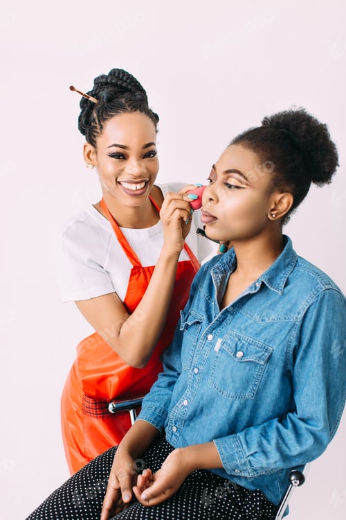 Preview: Young beautiful African American woman applying professional make-up by African make-up artist