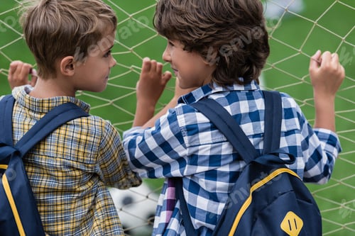 Preview: back view of two little schoolboys standing near soccer gate and looking at each other