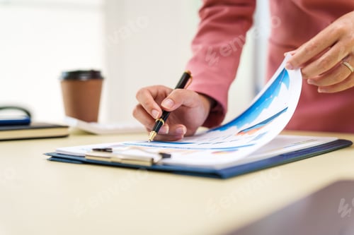 Preview: A businesswoman in a pink suit works at a desk with a whiteboard in the background.