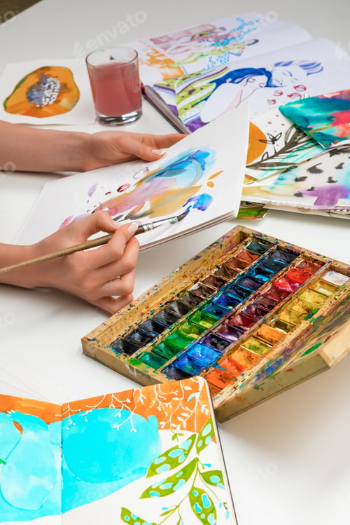 Preview: selective focus of female hands painting with watercolors paints and paintbrush on white album