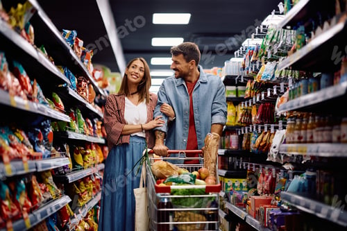 Preview: Happy couple with shopping cart walking through supermarket.