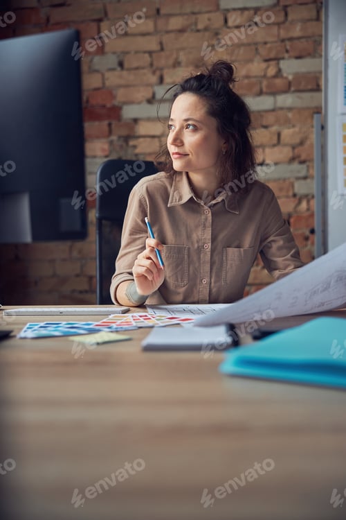 Preview: Cheerful female interior designer smiling away while working with drawing, material sample in her