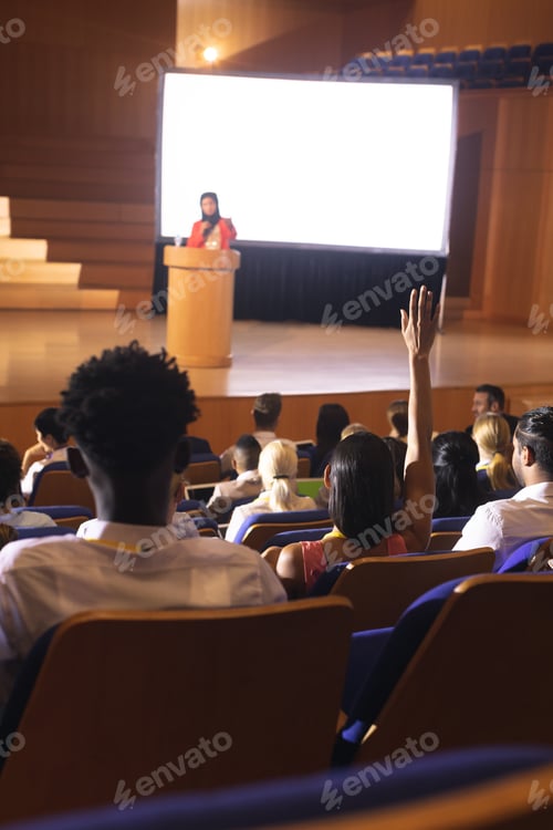 Preview: Front view of mixed race woman sitting in audience raising hand for asking question