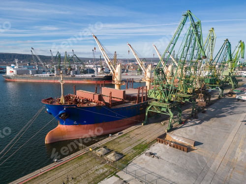 Preview: A bulk carrier ship loaded with grain is docked at a busy port, with workers and machinery seen in