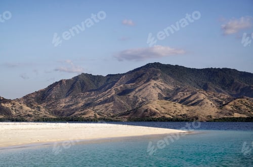 Preview: Empty white sand beach with blue ocean during the day overlooking mountain landscape with green