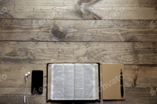 Preview: Overhead shot of a opened bible in the middle of a notebook and a smartphone on a wooden table