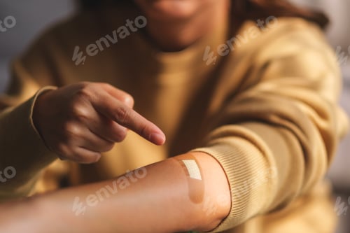 Preview: Woman pointing finger at a adhesive bandage, medical plaster, band aid on her arm