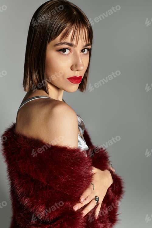 Preview: Stylish young woman with striking makeup posing confidently against a neutral background
