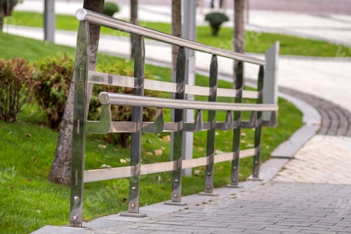 Preview: Metal fence construction made of shiny wet stainless pipes along road highway turn