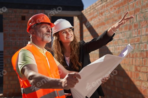 Preview: Cheerful female architect and her partner looking at building plans