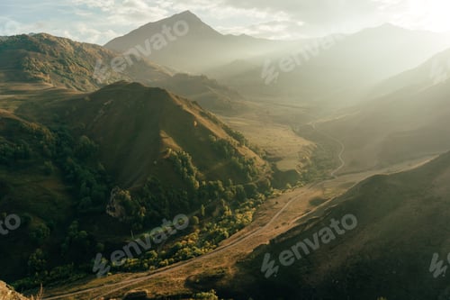 Preview: Sunset rays illuminate landscape view of a mountain pass, a rural road among the mountains.