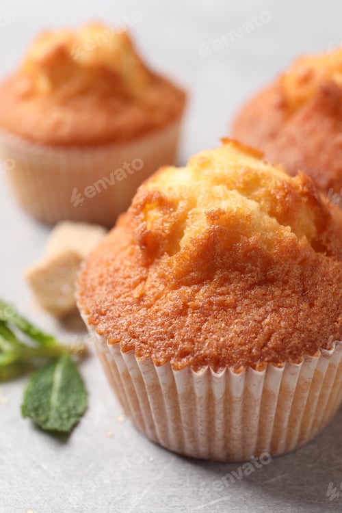 Preview: Delicious sweet muffins on light grey textured table, closeup