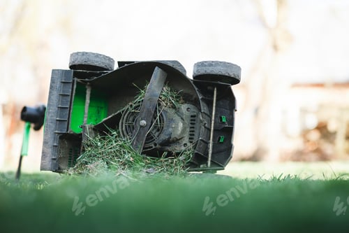 Preview: Lawn mower overflowing with grass lies on its side