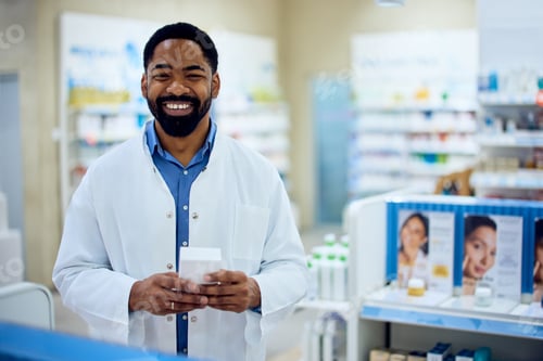 Preview: Smiling Pharmacist Standing in a Modern Pharmacy Holding a Medication Box