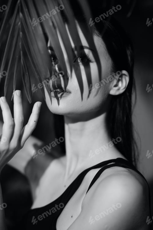 Preview: Mysterious woman with palm leaves covering her face in black and white photo under natural light