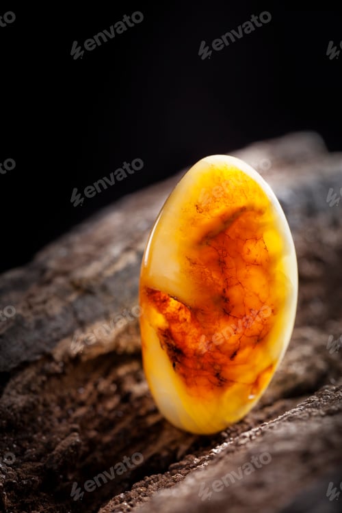 Preview: Natural amber. A piece of yellow opaque natural amber on large piece of dark stoned wood