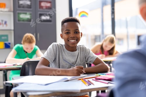 Preview: Portrait of smiling african american schoolboy working at his desk in class, copy space