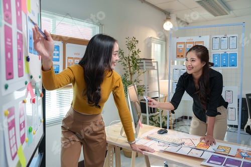 Preview: Two happy female web designers are discussing and working together on a new mobile app in a modern o