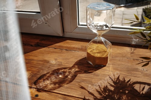 Preview: Hourglass with golden sand pouring inside on wooden background